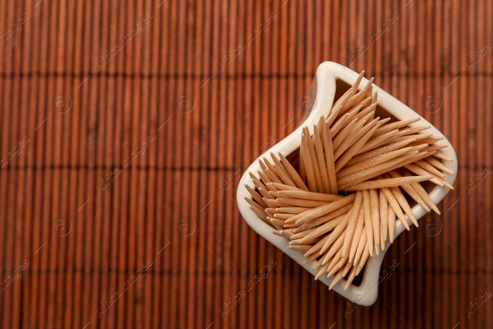 Photo of Holder with many toothpicks on bamboo mat, top view. Space for text