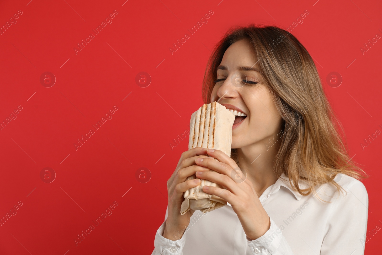 Photo of Young woman eating delicious shawarma on red background, space for text