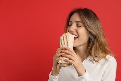 Photo of Young woman eating delicious shawarma on red background, space for text