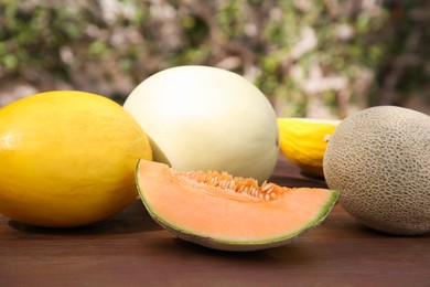 Photo of Whole and cut ripe melons on wooden table outdoors