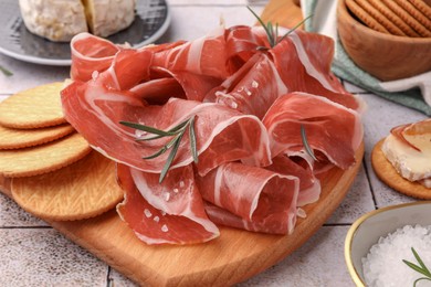 Photo of Slices of tasty cured ham, crackers and rosemary on tiled table, closeup