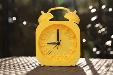 Yellow alarm clock on table outdoors at sunny morning