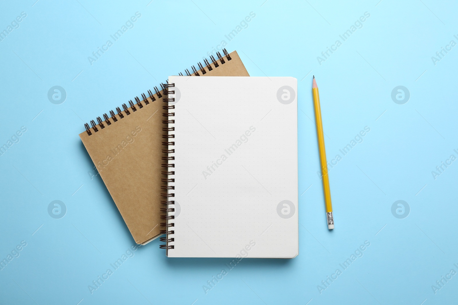 Photo of Notebooks and pencil on light blue background, top view