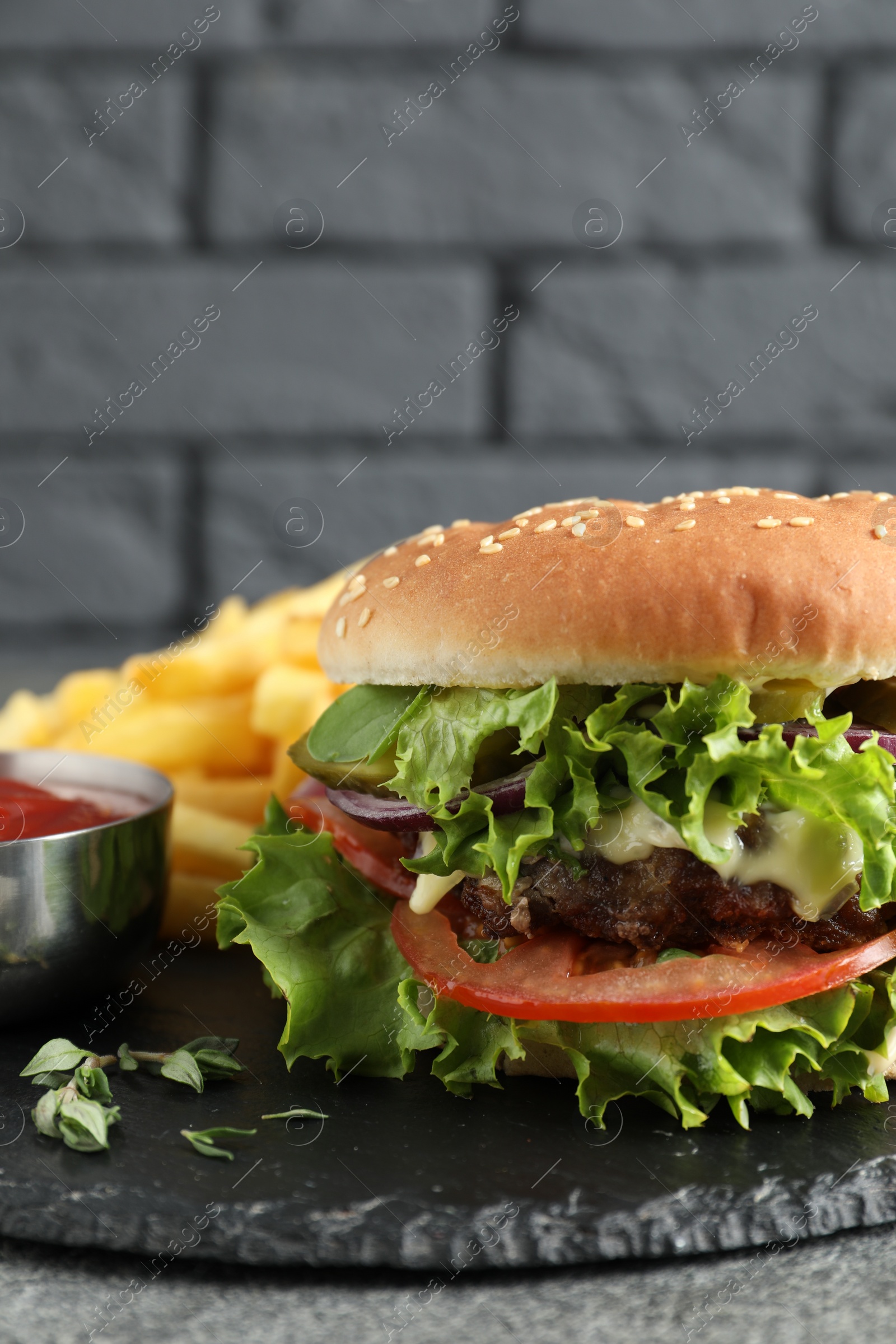 Photo of Delicious burger with beef patty, tomato sauce and french fries on grey table, closeup