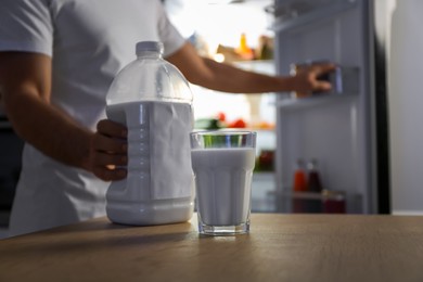 Photo of Man holding gallon bottle of milk and glass on wooden table in kitchen at night, closeup