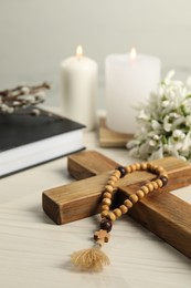 Church candles, wooden cross, rosary beads and Bible on white table