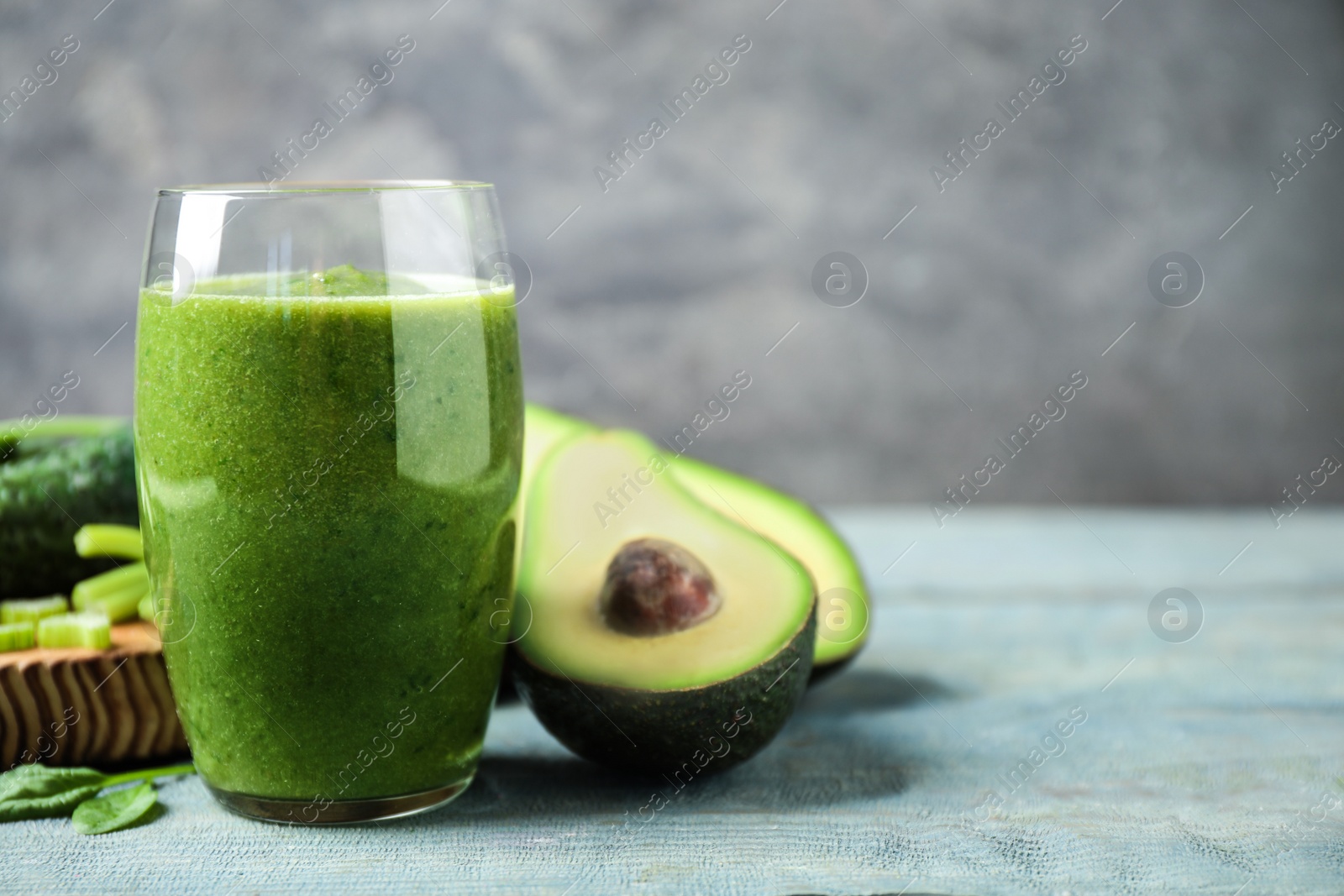 Photo of Delicious green juice and fresh ingredients on light blue wooden table, space for text
