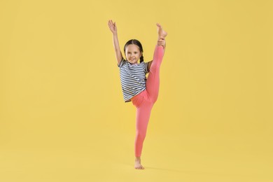 Photo of Cute little girl stretching on yellow background