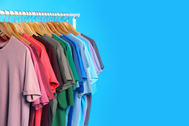 Photo of Colorful clothes hanging on rack against light blue background. Space for text