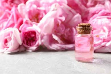 Photo of Bottle of rose essential oil and fresh flowers on grey table, space for text