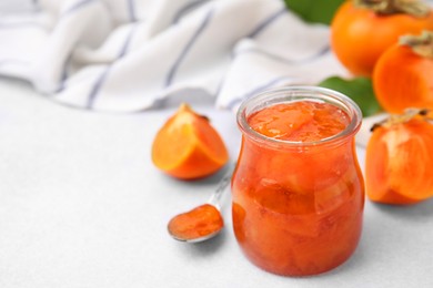 Jar of tasty persimmon jam and ingredients on white table. Space for text