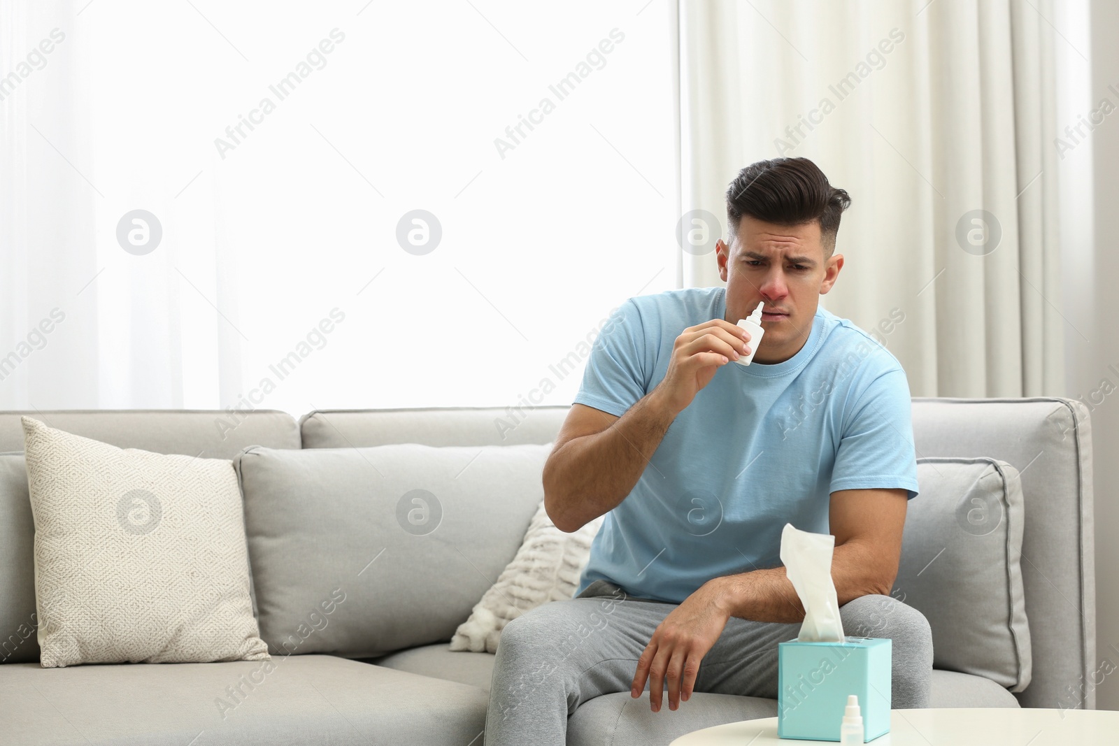 Photo of Ill man using nasal spray on sofa at home