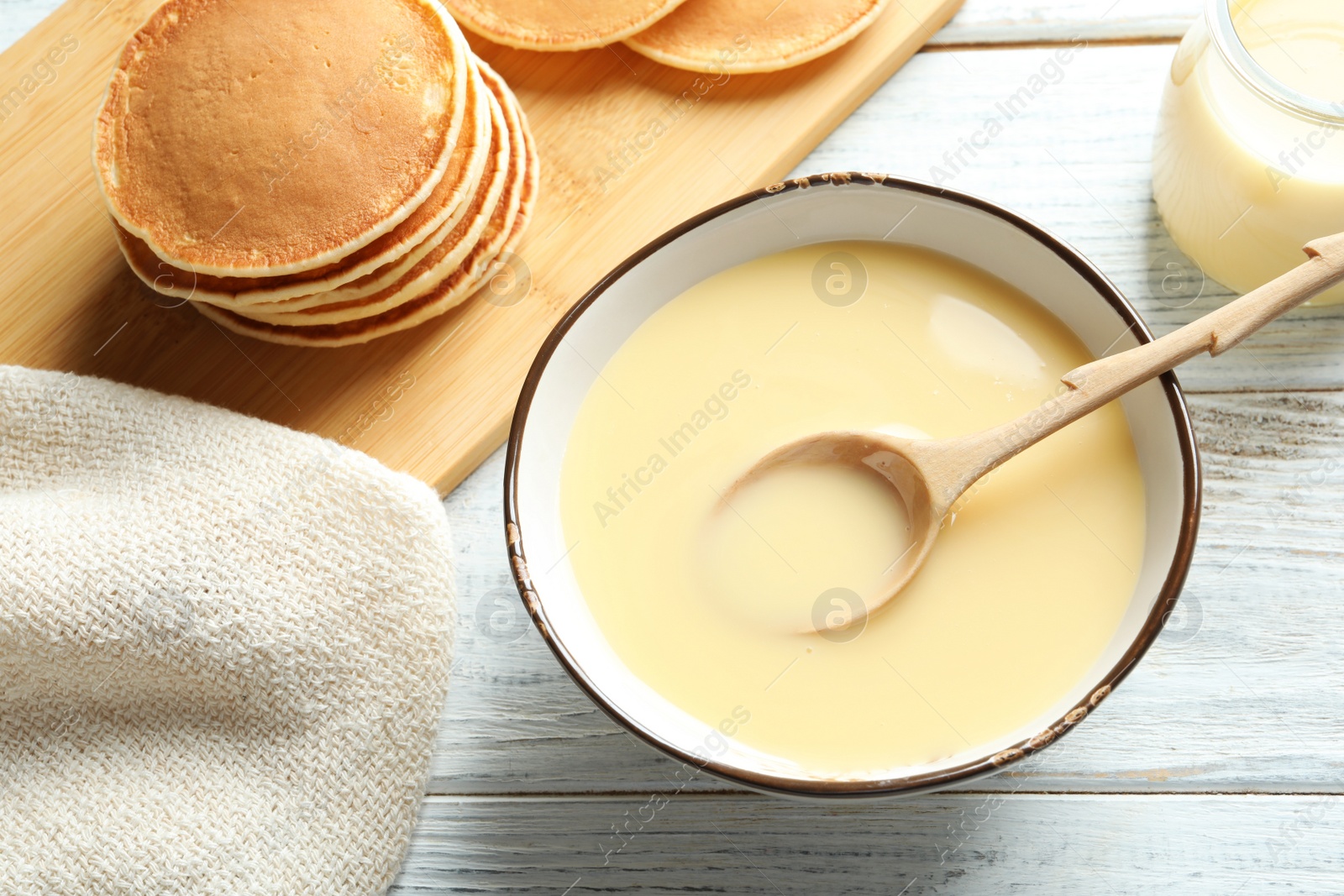 Photo of Bowl with condensed milk and served on wooden table, top view. Dairy products