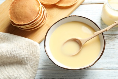 Bowl with condensed milk and served on wooden table, top view. Dairy products