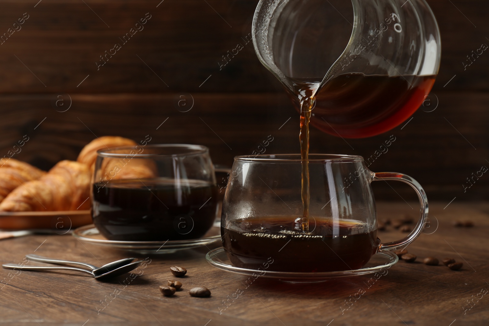 Photo of Pouring coffee into glass cup at wooden table, closeup