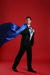 Businessman in superhero cape taking suit off on red background