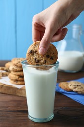 Photo of Woman dipping delicious chocolate chip cookie into glass of milk at wooden table, closeup