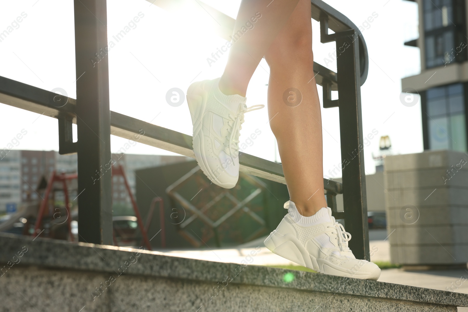 Photo of Woman wearing stylish sneakers near railing outdoors, closeup