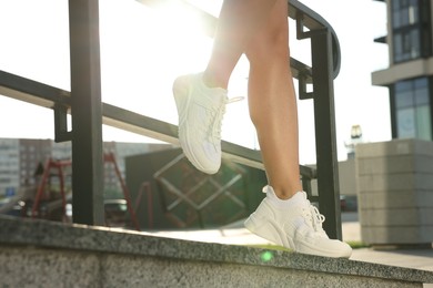 Photo of Woman wearing stylish sneakers near railing outdoors, closeup