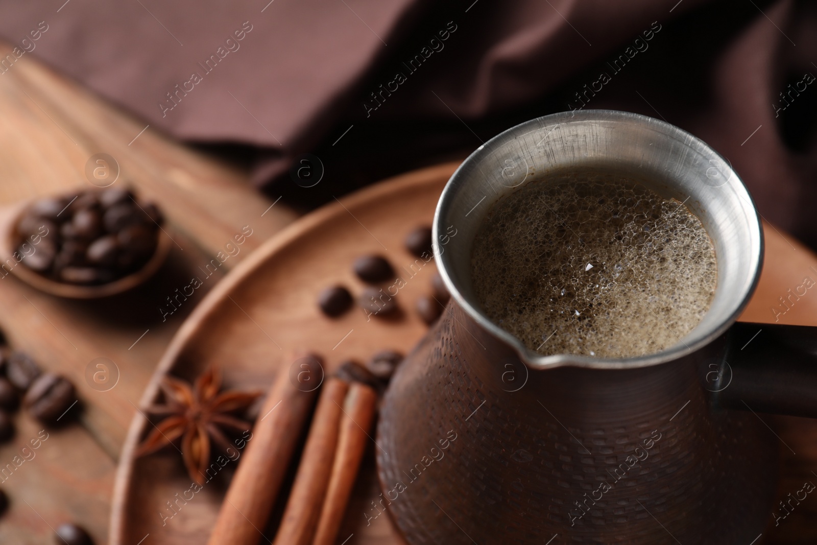 Photo of Cezve with Turkish coffee, beans and spices on wooden table, closeup. Space for text