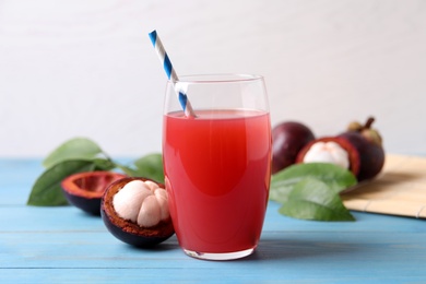 Photo of Delicious fresh mangosteen juice in glass on light blue wooden table