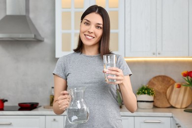 Woman with jug and glass of water in kitchen