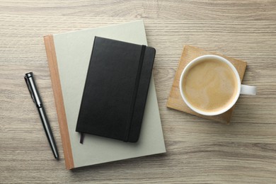 Photo of Different notebooks, pen and cup of coffee on wooden table, flat lay