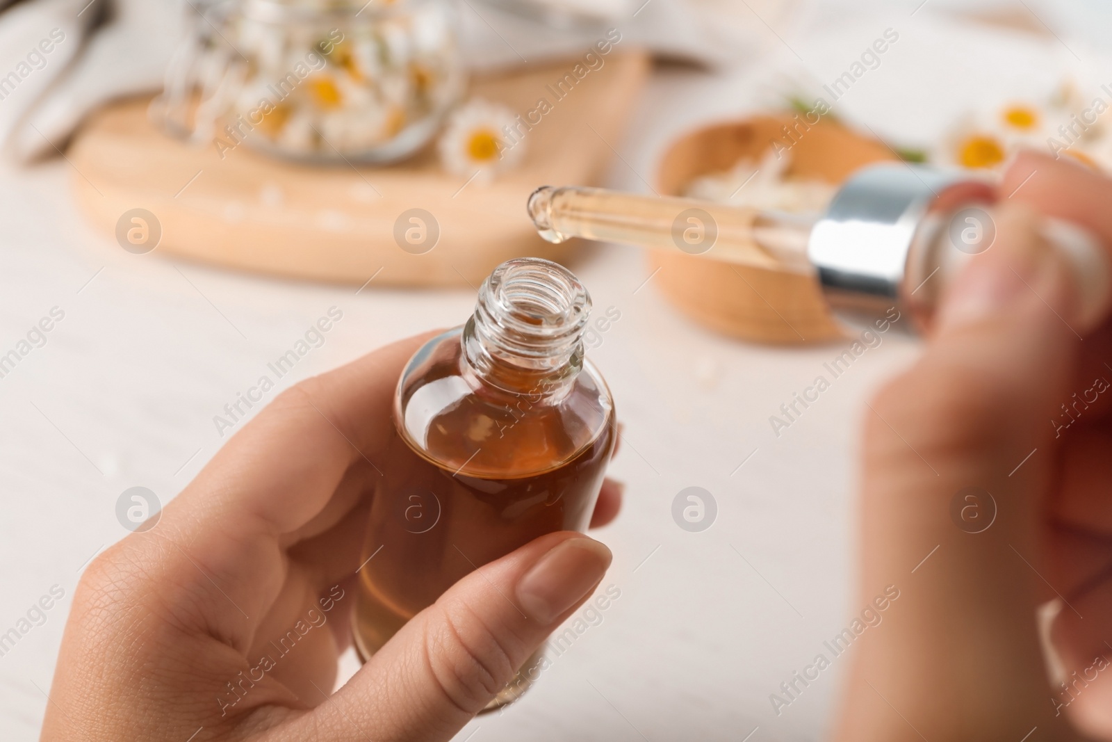 Photo of Woman holding bottle and pipette with essential oil over table, closeup