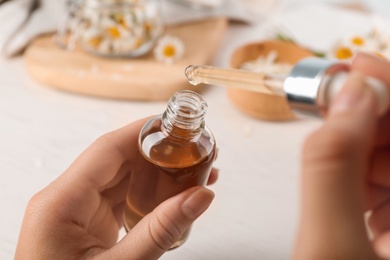 Woman holding bottle and pipette with essential oil over table, closeup