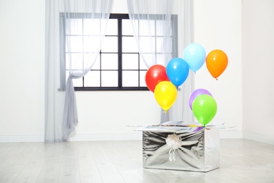 Photo of Gift box with bright air balloons on floor indoors. Space for text