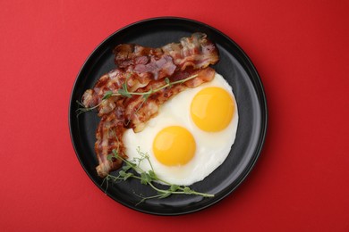 Photo of Fried eggs, bacon and microgreens on red background, top view