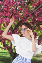 Photo of Attractive young woman posing near blossoming tree on sunny spring day