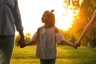 Little girl and her parents holding hands in park. Happy family
