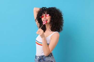 Beautiful woman in sunglasses with lollipop on light blue background