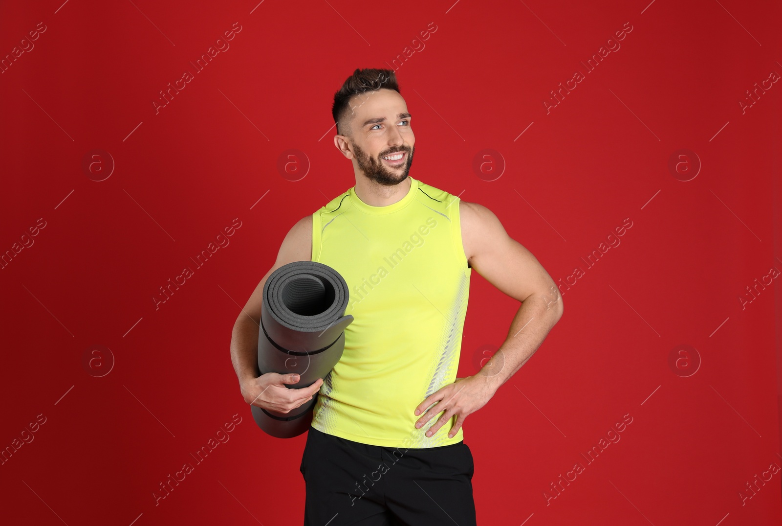 Photo of Handsome man with yoga mat on red background