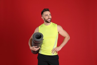 Photo of Handsome man with yoga mat on red background