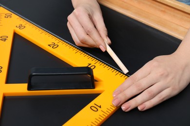 Photo of Woman drawing with chalk and triangle ruler on blackboard, closeup