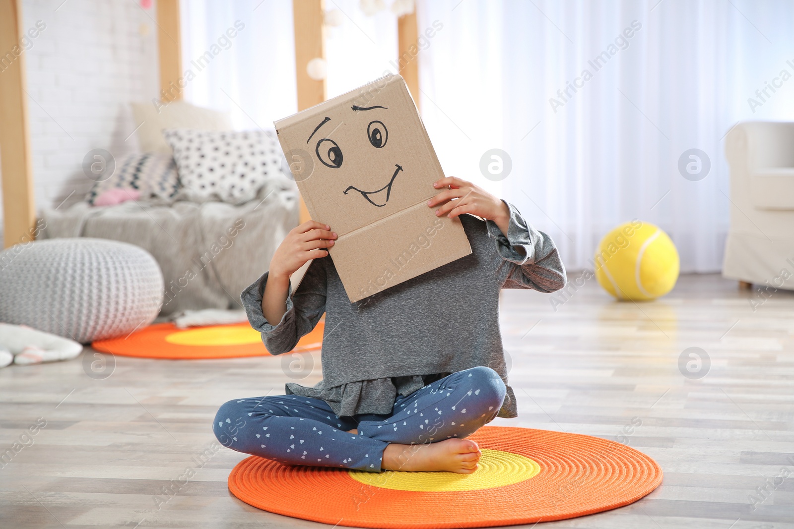 Photo of Cute little child wearing cardboard box with smiling face in bedroom