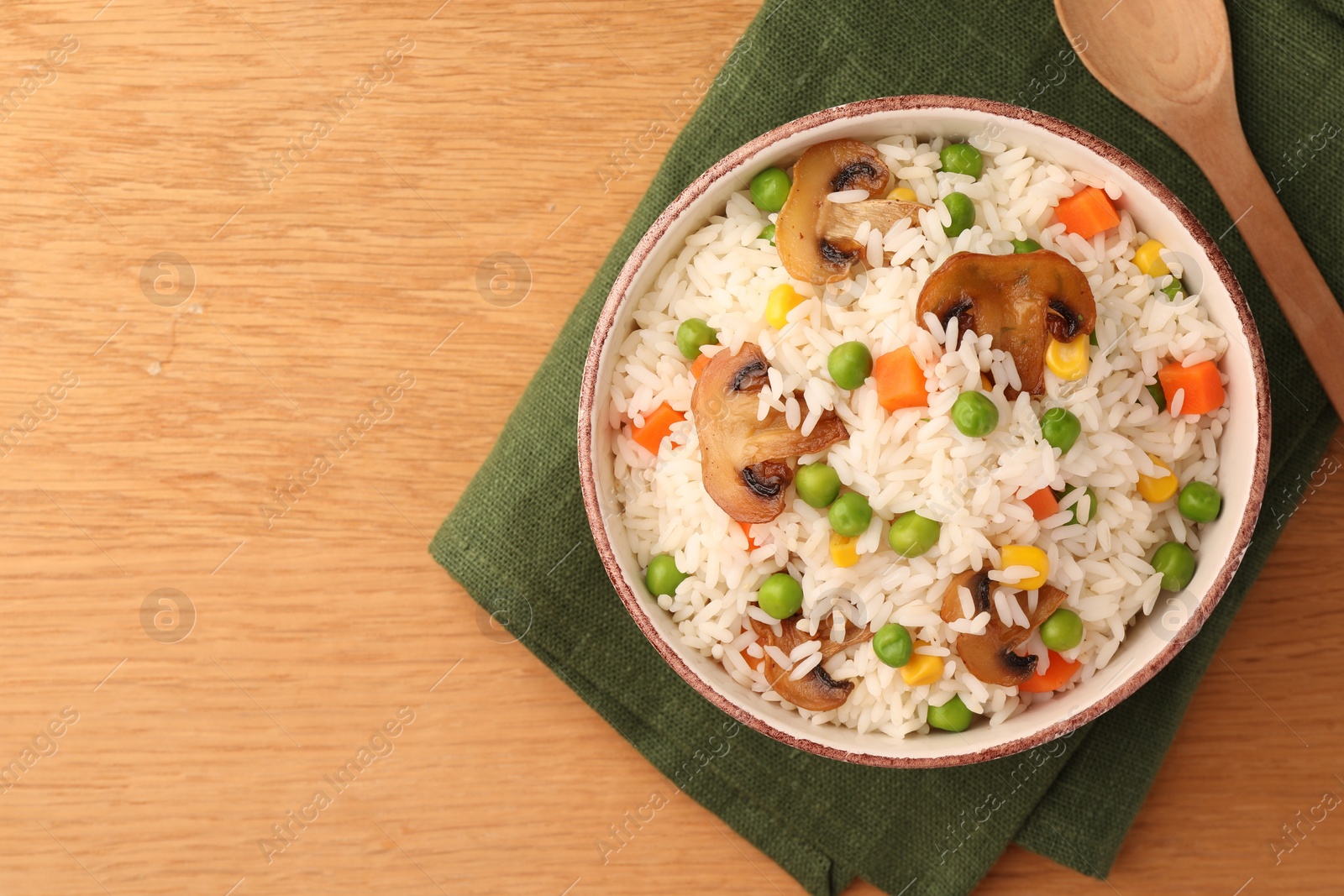 Photo of Bowl of delicious rice with vegetables on wooden table, top view. Space for text