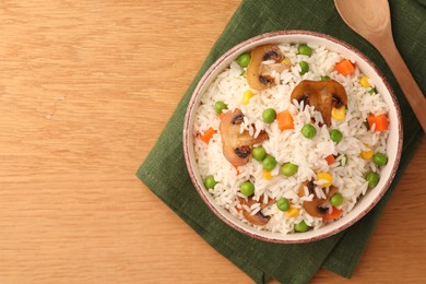 Photo of Bowl of delicious rice with vegetables on wooden table, top view. Space for text