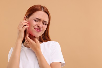 Photo of Suffering from allergy. Young woman scratching her face on beige background, space for text
