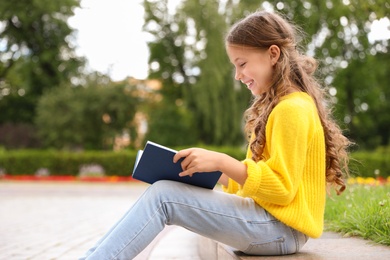 Cute little girl reading book in green park