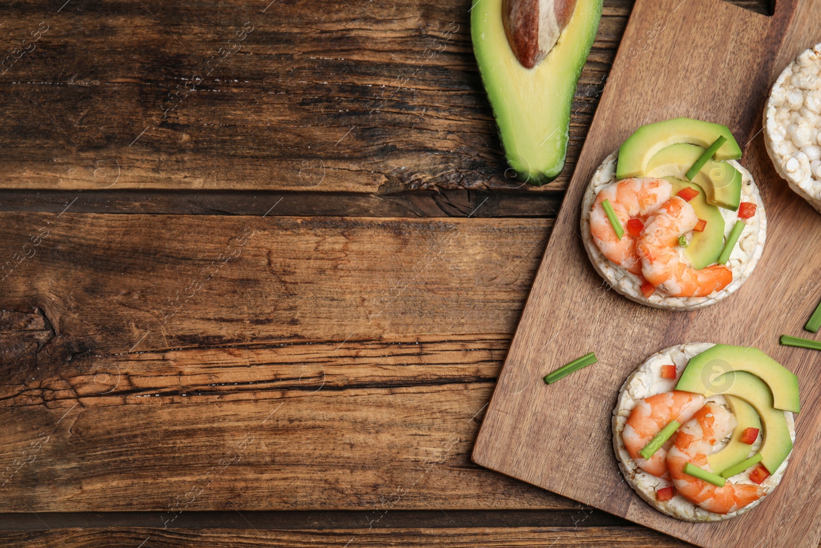 Photo of Puffed rice cakes with shrimps and avocado on wooden table, flat lay. Space for text