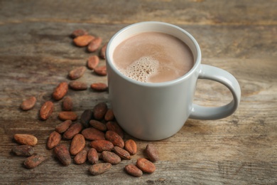 Photo of Cup with hot chocolate drink and cocoa beans on wooden table