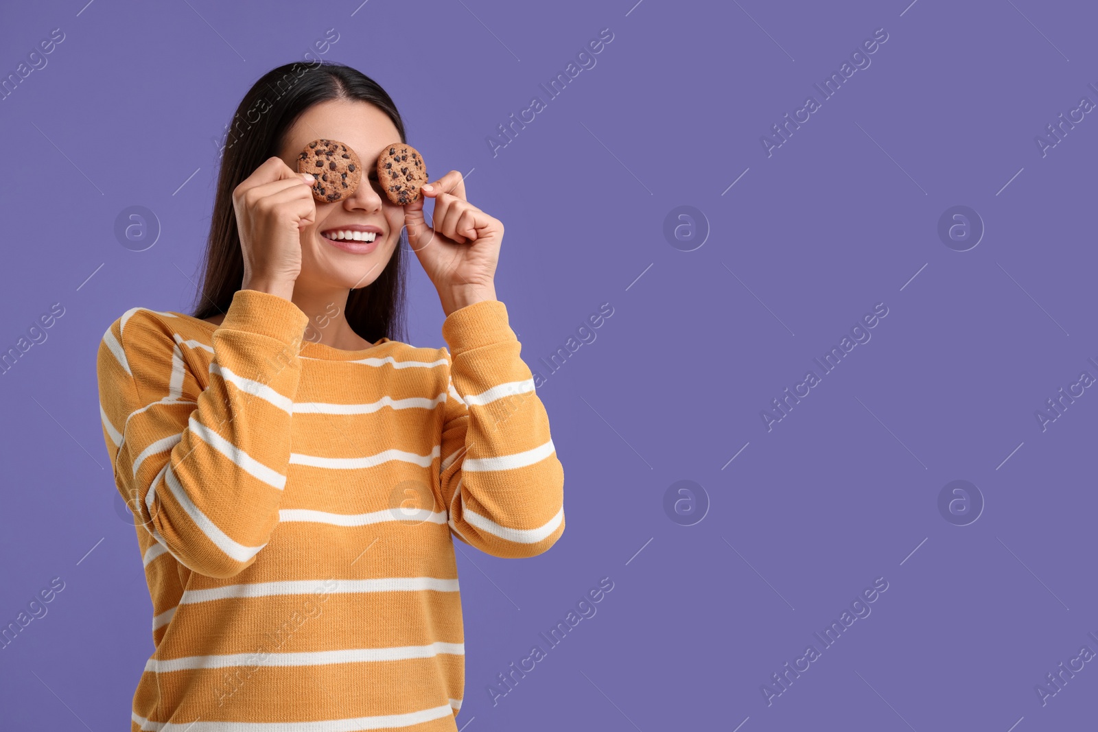Photo of Young woman with chocolate chip cookies on purple background, space for text