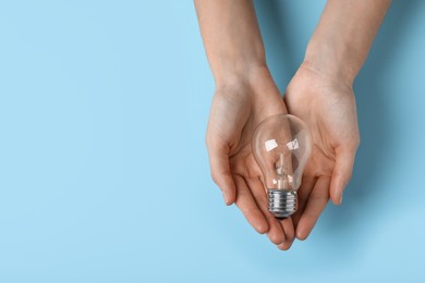 Photo of Woman holding light bulb on color background, top view. Space for text