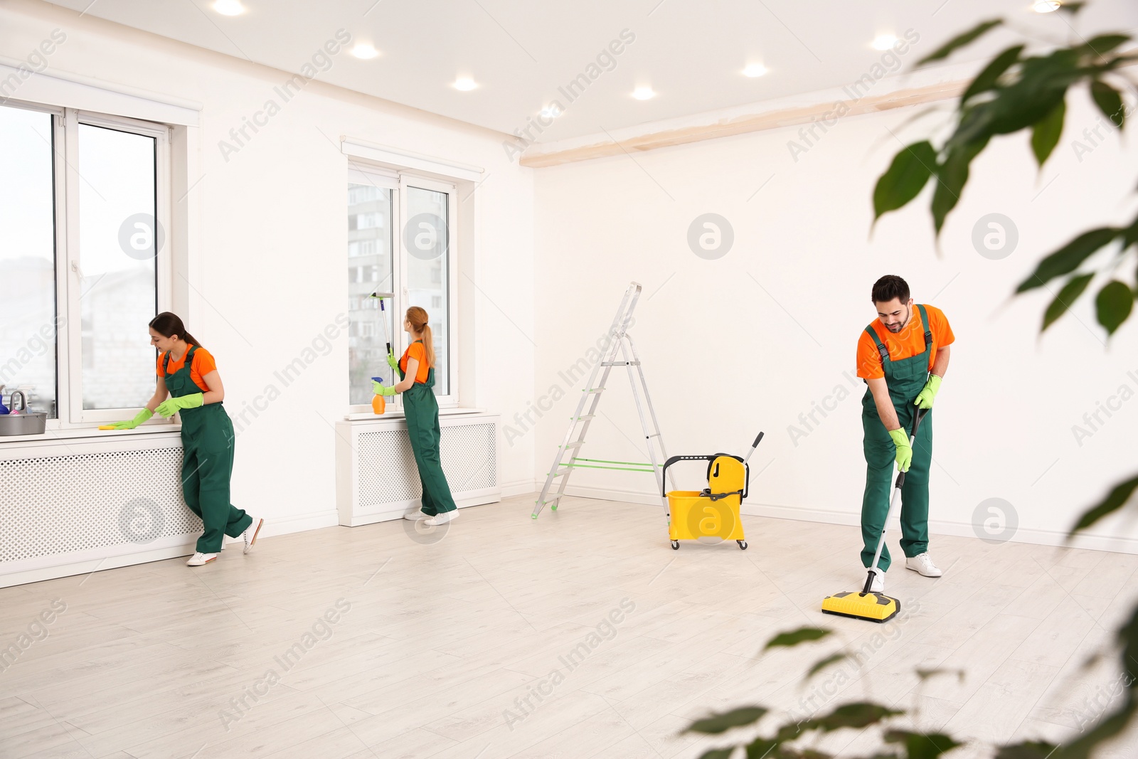 Photo of Team of professional janitors in uniforms cleaning room