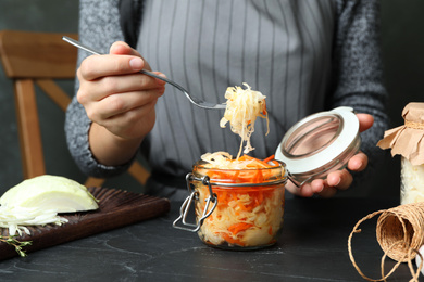 Photo of Woman eating fermented cabbage at black table, closeup