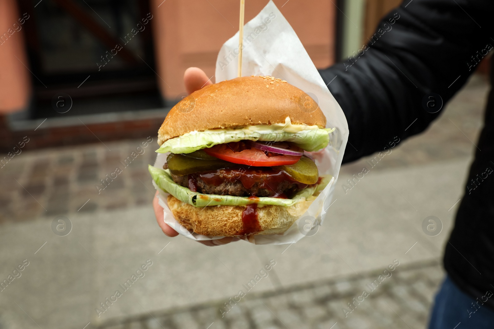 Photo of Woman holding fresh delicious burger outdoors, closeup. Street food