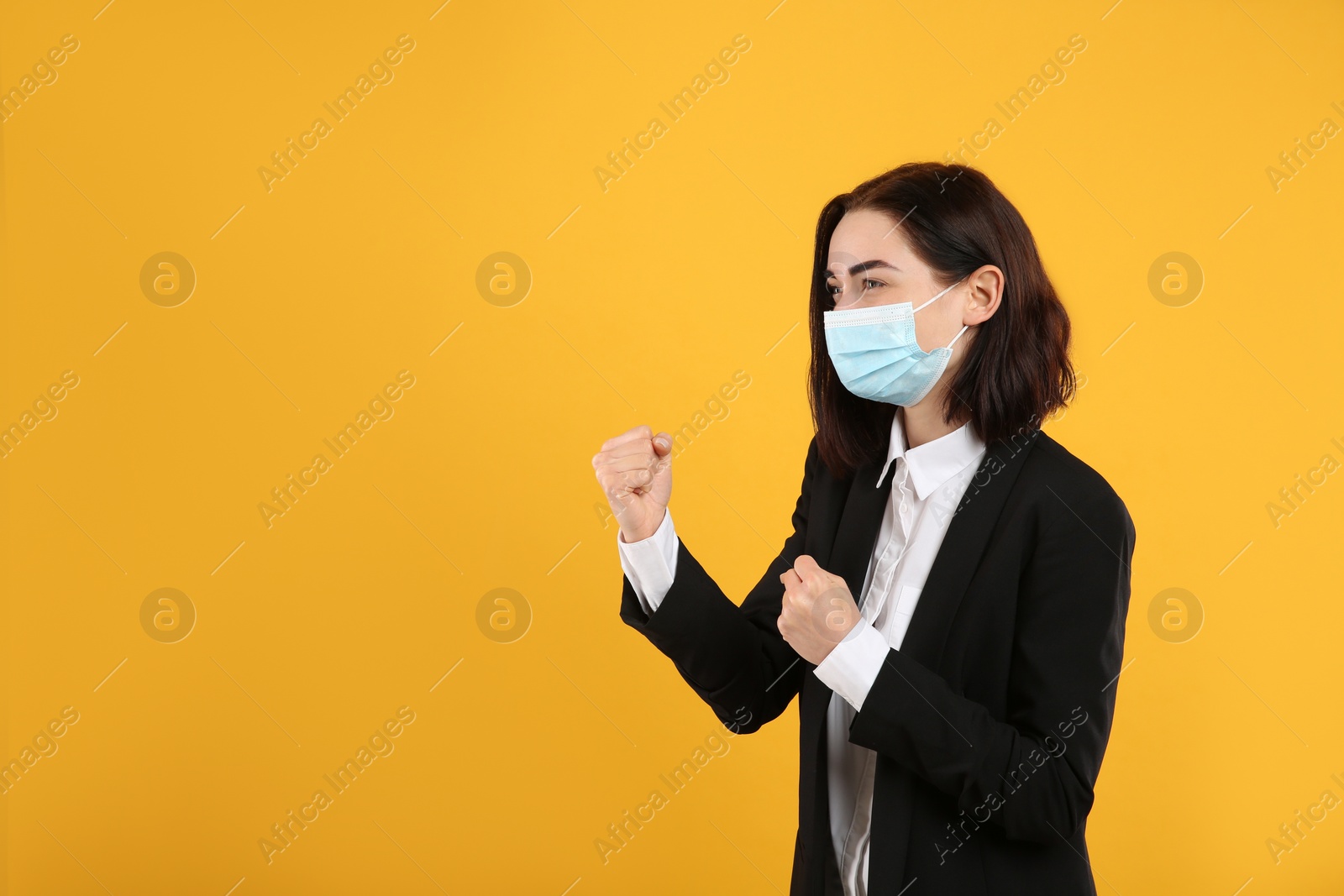 Photo of Businesswoman with protective mask in fighting pose on yellow background, space for text. Strong immunity concept